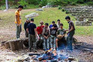 Troop 23 Scouts gathered around an established stone fire ring with a small fire burning, Camp Seton, Greenwich, Connecticut