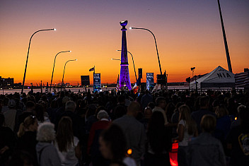 The crowd at the 9/11 vigil on the American Veterans Memorial Pier at dusk, with the Beacon memorial lit against an orange sky, Bay Ridge, Brooklyn, September 11, 2025
