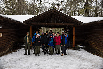 Troop 23 Brooklyn Scouts and adult leaders in front of a cabin in the snow at Ten Mile River Scout Camps, February 2025 winter weekend