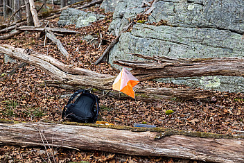An orange-and-white orienteering control flag beside a backpack among rocks and fallen logs on the Surebridge course, Harriman State Park, January 4, 2025