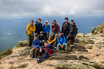 The whole party — scouts and adult leaders — on the summit ridge of Katahdin with the lakes and forest of Baxter State Park thousands of feet below, on the way down from Baxter Peak, Tuesday of Troop 23 Brooklyn's Adventure Trek, August 11, 2026