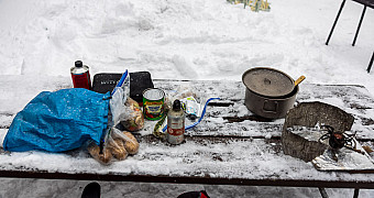 Camp stoves, a pot and food laid out on a snow-covered table during Troop 23 Brooklyn's winter weekend at Massawepie Scout Camps, Adirondacks, January 2026