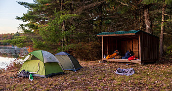A wooden lean-to with sleeping bags inside and two tents beside it on the shore of Crystal Lake, Lakeside Lean-Tos site B, Ten Mile River Scout Camps, October 2025