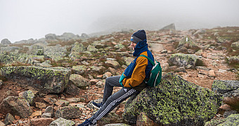 The Cloud Lifting on the Descent — Katahdin A scout resting on a boulder as the cloud begins to lift on the way down from Baxter Peak, the trail and the rocks emerging behind him, Tuesday of Troop 23 Brooklyn's Adventure Trek, August 11, 2026