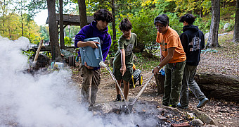 Troop 23 Scouts drowning a campfire with water as steam rises from the fire ring, Camp Seton
