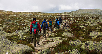 The Tableland — Katahdin Scouts walking in single file across the Tableland, the nearly flat alpine tundra plateau at about 4,600 feet on Katahdin — low mats and grasses, scattered granite, a cairn marking the route under heavy cloud, Tuesday of Troop 23 Brooklyn's Adventure Trek, August 11, 2026