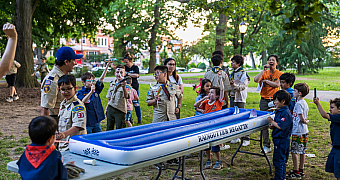 Raingutter Regatta in Owl's Head Park Cub Scouts of Pack 23 and Scouts of Troop 23 crowd around an inflatable Raingutter Regatta course on folding tables in Owl's Head Park, Bay Ridge, June 2024