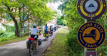 Bikepacking the Empire State Trail — Erie Canalway Riders of the 2025 Adventure Trek with loaded panniers on the Erie Canalway section of the Empire State Trail, New York, past the trail's signs