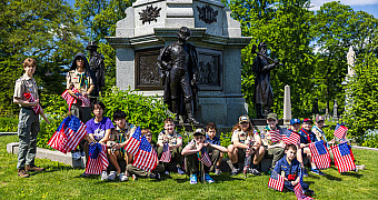 At the Civil War Soldiers' Monument Scouts and Cub Scouts with small American flags sit and stand at the foot of the Civil War Soldiers' Monument on Battle Hill in Green-Wood Cemetery, Brooklyn, May 2025