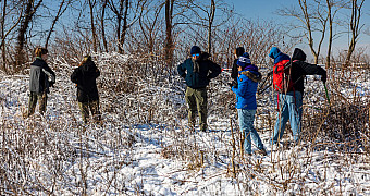 Scouts cut back snow-covered brush with loppers near the shore of Conference House Park, Staten Island, with the water behind them, January 2026