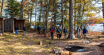 Scouts crossing the Lakeside Lean-Tos site between the lean-tos and the fire ring, with Crystal Lake behind the trees, Ten Mile River Scout Camps, October 2025